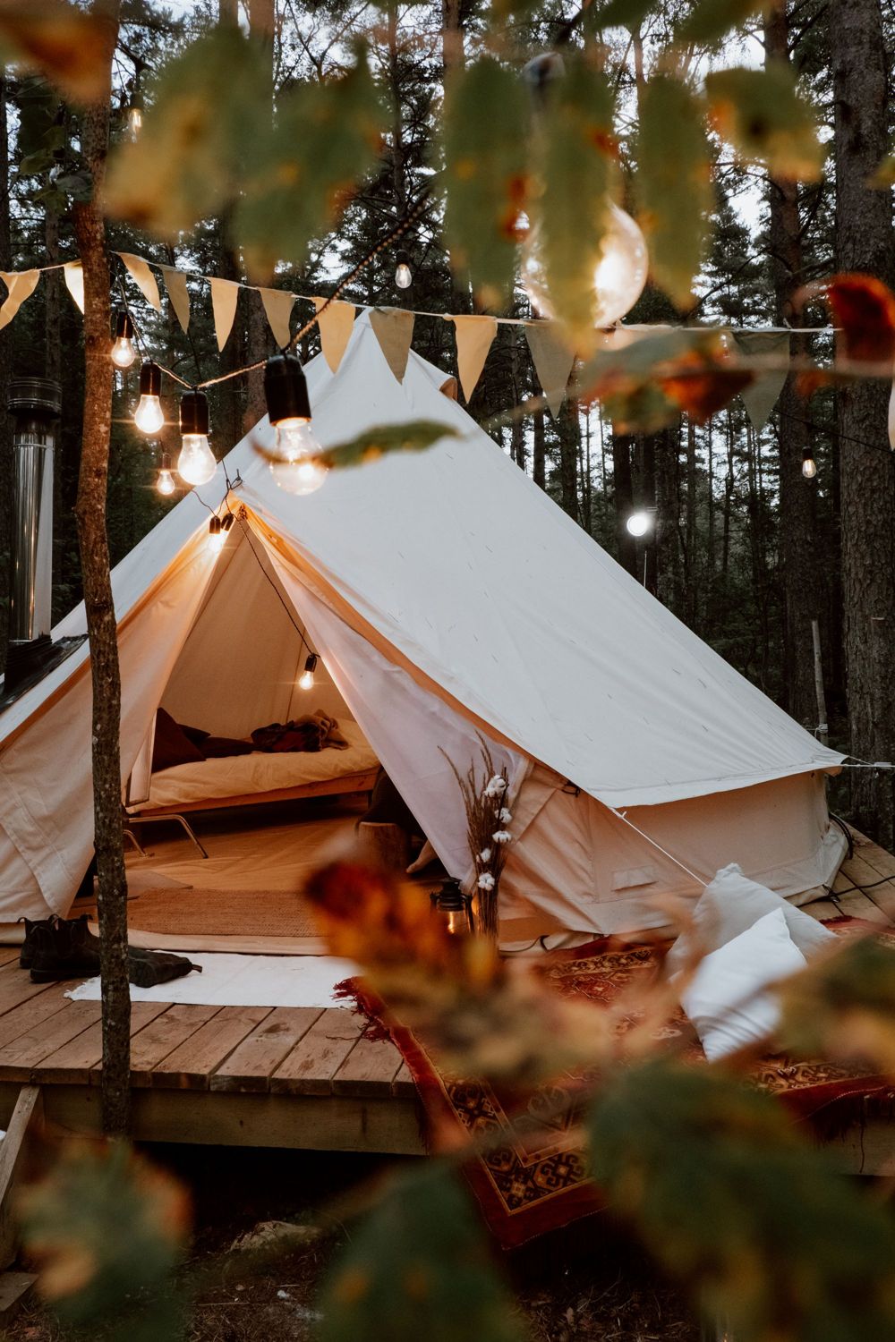 A furnished canvas tent under warm lights in a wooded setting, illustrating the glamping experience